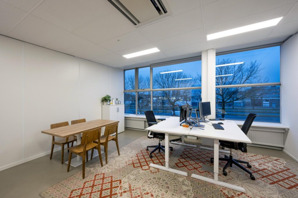 Modern ingericht kantoor aan de Van der Madeweg met twee bureaus, een vergadertafel en grote ramen met uitzicht op de straat.